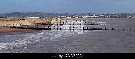 Ankommende Flut und Groynen am Dawlish Warren Strand, mit Blick auf den fernen Exmouth. Stockfoto