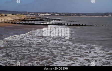 Ankommende Flut und Groynen am Dawlish Warren Strand, mit Blick auf den fernen Exmouth. Stockfoto