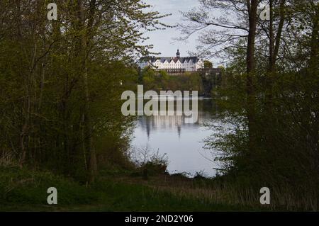 Das Plon-Schloss in Deutschland spiegelt sich im Wasser zwischen den Bäumen wider Stockfoto