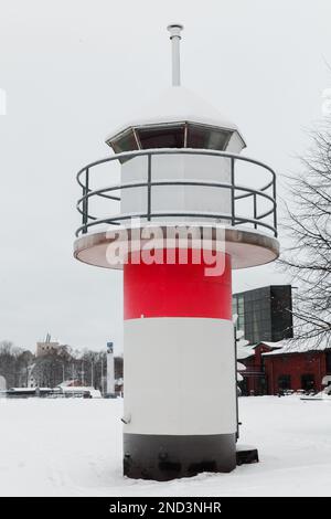 Weißer Leuchtturm mit roten Streifen steht an einem Wintertag an der Küste im Hafen von Turku, Finnland Stockfoto