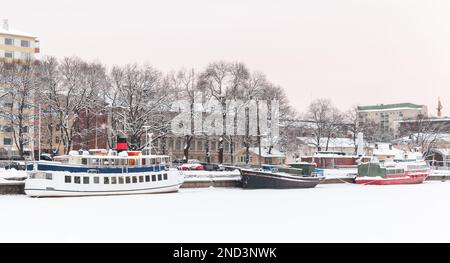 An einem Wintertag in Turku, Finnland, liegen kleine Boote an der Küste des Flusses Aura vor Stockfoto