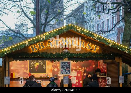 Nahaufnahme eines beleuchteten Schilds eines Bratwurststststalls in einem hölzernen Chalet im alpinen Stil auf den Manchester Christmas Markets. Manchester. UK Stockfoto