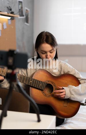 Online-Lernkonzept. Livestream-Video oder virtuelles Video-Tutorial für asiatische Gitarreninnen zu Hause, Blogger oder Vlogger für Künstler und Musiker am Tisch Stockfoto