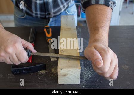 Bild der Hände eines Zimmermanns, der ein Stück Holz mit einer Raspel glättet. Holzfeilen und -Reinigung. Stockfoto