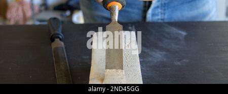 Bild eines Handwerkers, der beim Arbeiten und Schnitzen von Holz mit einem Schreinerhammer und Meißel arbeitet. Heimwerkerarbeit im Labor. Stockfoto