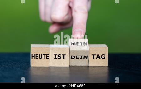 Die Hand würfelt und ändert den deutschen Ausdruck „heute ist dein Tag“ (heute ist dein Tag) in „heute ist mein Tag“ (heute ist mein Tag). Stockfoto