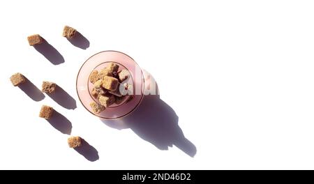 Viele braune Zuckerwürfel in einer Teetasse und Untertasse auf weißem Hintergrund, Nahaufnahme von oben, Studioaufnahme Stockfoto