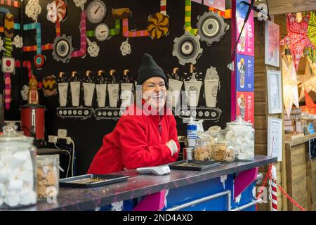 Eine glückliche Weiße hinter der Theke eines Stalls, der heiße Schokoladengetränke auf dem Weihnachtsmarkt der St. Nicholas Fair verkauft. Nach York. Stockfoto