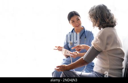 Glückliche Seniorin, deren Blutdruck in einem Pflegeheim von ihrer Pflegekraft gemessen wird. Glückliche Krankenschwester, die den Blutdruck einer Seniorin misst Stockfoto