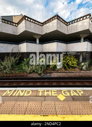 Schild auf dem Boden der U-Bahnstation West London, „Mind the Gap“; 1970er Wohnblock im Hintergrund Stockfoto