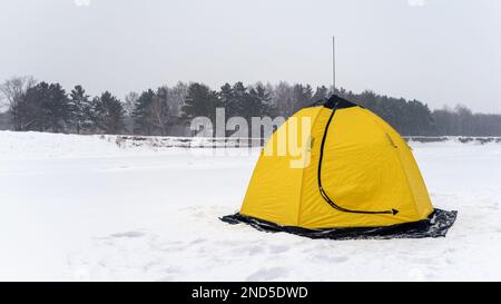 Gelbe Angeln winter Zelt in Form eines Lotus steht auf dem verschneiten Eis des Flusses geschlossen gegen den verschneiten Wald Bäume im Winter. Stockfoto