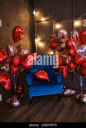 Innenausstattung im Loft-Stil mit blauem Sessel, dekoriert mit vielen herzförmigen Ballons für Valentinstag oder andere romantische oder festliche Veranstaltungen. Sei besonders Stockfoto