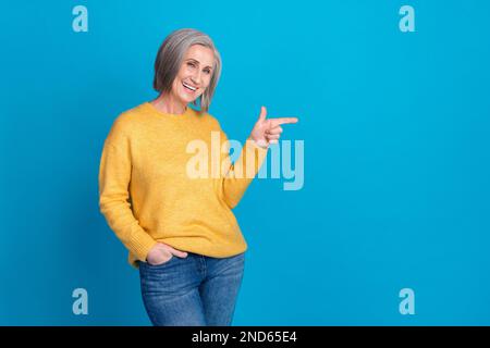 Foto einer hinreißenden Seniorin mit selbstbewusster Pose, leerer Raum, elegantes gelbes Outfit, isoliert auf blauem Hintergrund Stockfoto