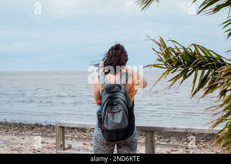 Rückansicht einer unbekannten jungen Frau, mit Rucksack auf dem Rücken, der vor dem Meer steht, Reisekonzept, Kopierraum. Stockfoto