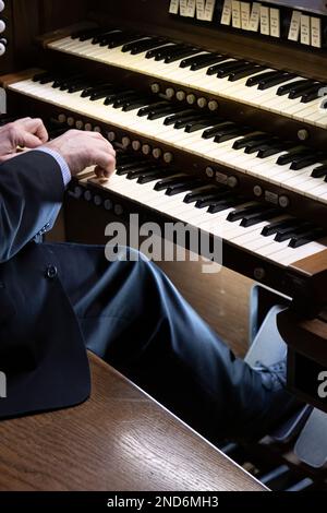 Eine Nahaufnahme eines Mannes, der die schwarz-weißen Klaviertasten einer Pfeifenorgel in der Kirche spielt Stockfoto