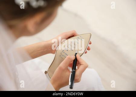 Die junge Braut schreibt die Namen ihrer Single-Freunde drinnen, über dem Bild. Hochzeitsabergläubisch Stockfoto