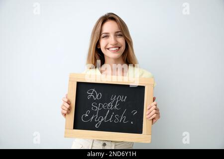 Junge Lehrerin mit Tafel und Wörtern Sprechen sie Englisch? Auf hellem Hintergrund Stockfoto
