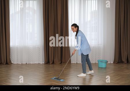 Junge Frau, die den Boden mit Mopp in einem leeren Raum putzt Stockfoto