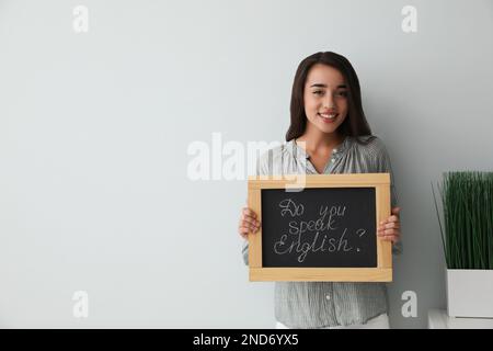 Junge Lehrerin mit Tafel und Wörtern Sprechen sie Englisch? Auf hellem Hintergrund. Platz für Text Stockfoto
