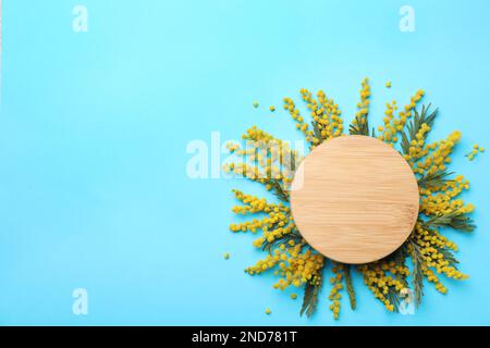 Wunderschöne Blumenzusammensetzung mit Mimosablumen und Holzbrett auf hellblauem Hintergrund, flach liegend. Platz für Text Stockfoto