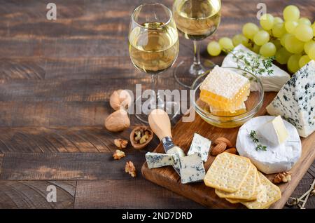 Käseplatte mit Trauben, Cracker, Honig und Nüssen auf einem Holztisch. Stockfoto