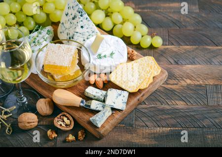 Käseplatte mit Trauben, Cracker, Honig und Nüssen auf einem Holztisch. Stockfoto