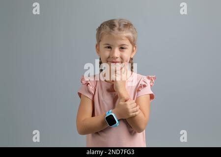 Kleines Mädchen mit Smartwatch auf grauem Hintergrund Stockfoto