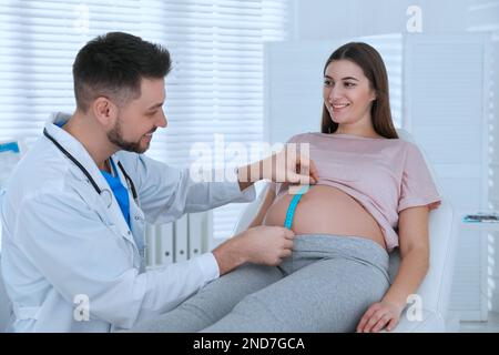 Der Arzt, der den Bauch einer schwangeren Frau mit Klebeband in der Klinik misst Stockfoto