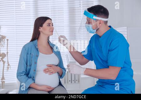 Arzt, der Nasenabstrich einer schwangeren Frau für den Coronavirus-Test in der Klinik nimmt Stockfoto