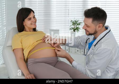 Der Arzt, der den Bauch einer schwangeren Frau mit Klebeband in der Klinik misst Stockfoto