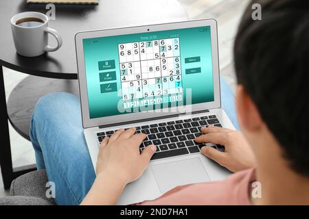 Ein Mann spielt Sudoku-Spiel auf einem Laptop drinnen, Nahaufnahme Stockfoto