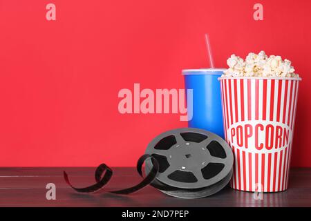 Köstliches Popcorn, Getränke und Filmrolle auf einem Holztisch. Platz für Text Stockfoto