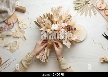 Ein Blumenhändler, der einen wunderschönen Strauß getrockneter Blumen am weißen Tisch zubereitet, mit Blick von oben Stockfoto