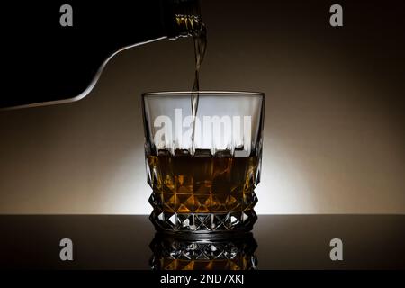 Whiskey wird in ein Glas mit Hintergrundbeleuchtung gegossen. Stockfoto