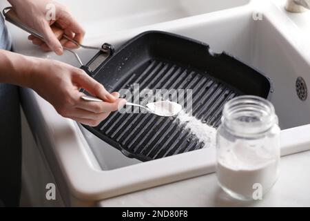 Frau, die Backpulver benutzt, um Pfanne drinnen zu grillen, Nahaufnahme Stockfoto