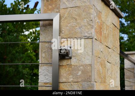 Zaunpfahl oder Pier aus Naturstein in strukturiertem Beige mit Edelstahltor und Scharnier. Geschweißter Vierkantrohrrahmen. Verdrillte Kabelschiene. Landschaftsbau. Stockfoto