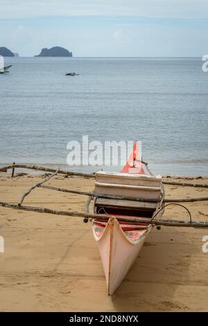 Dieses Foto zeigt die Essenz der Philippinen, mit einem traditionellen Holzboot, das auf kristallklarem türkisfarbenem Wasser wackelt, umgeben von üppigem Grün Stockfoto