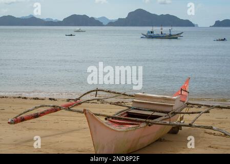 Dieses Foto zeigt die Essenz der Philippinen, mit einem traditionellen Holzboot, das auf kristallklarem türkisfarbenem Wasser wackelt, umgeben von üppigem Grün Stockfoto