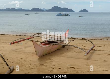 Dieses Foto zeigt die Essenz der Philippinen, mit einem traditionellen Holzboot, das auf kristallklarem türkisfarbenem Wasser wackelt, umgeben von üppigem Grün Stockfoto