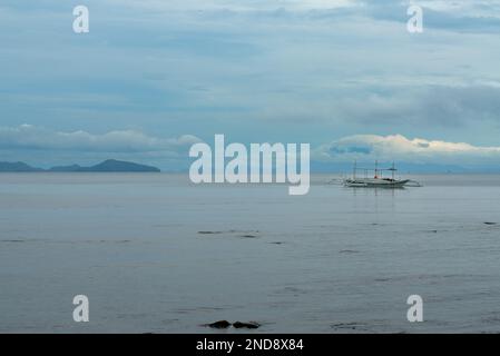 Dieses Foto zeigt die Essenz der Philippinen, mit einem traditionellen Holzboot, das auf kristallklarem türkisfarbenem Wasser wackelt, umgeben von üppigem Grün Stockfoto