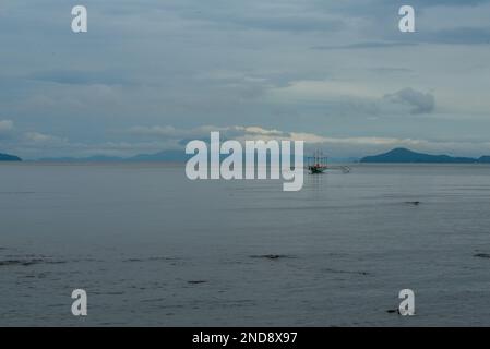 Dieses Foto zeigt die Essenz der Philippinen, mit einem traditionellen Holzboot, das auf kristallklarem türkisfarbenem Wasser wackelt, umgeben von üppigem Grün Stockfoto