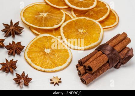 Zimtstäbchen in einem Bündel mit einem braunen Band. Sternanis und trockene Orangenscheiben. Weißer Hintergrund. Stockfoto