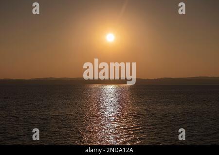 Wunderschöner Sonnenuntergang über dem atemberaubenden Gardasee in Italien, mit der Sonne, die auf dem ruhigen Wasser reflektiert, und einer friedlichen Atmosphäre. Perfekt für Trav Stockfoto