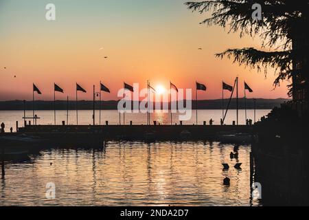 Wunderschöner Sonnenuntergang über dem atemberaubenden Gardasee in Italien, mit der Sonne, die auf dem ruhigen Wasser reflektiert, und einer friedlichen Atmosphäre. Perfekt für Trav Stockfoto