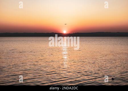 Wunderschöner Sonnenuntergang über dem atemberaubenden Gardasee in Italien, mit der Sonne, die auf dem ruhigen Wasser reflektiert, und einer friedlichen Atmosphäre. Perfekt für Trav Stockfoto