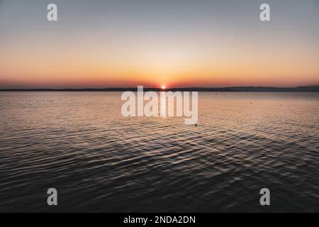 Wunderschöner Sonnenuntergang über dem atemberaubenden Gardasee in Italien, mit der Sonne, die auf dem ruhigen Wasser reflektiert, und einer friedlichen Atmosphäre. Perfekt für Trav Stockfoto