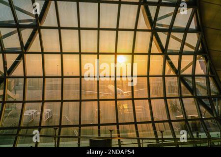 Malerischer Sonnenaufgang über dem Flugzeug Stehen Sie still auf dem Suvarnabhumi Flughafen, von innen durch den Fensterrahmen gesehen Stockfoto