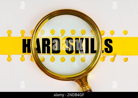 Zwischen zwei Blättern aus einem Notizbuch auf einem gelben Streifen mit der Aufschrift „HARD SKILLS“ befindet sich eine Lupe. Geschäftskonzept. Stockfoto