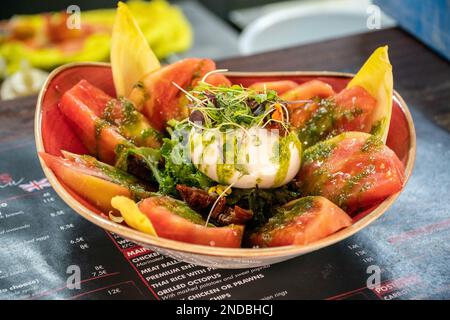 Ein Bild eines Burrata-Käsesalats gefüllt mit saftigen Tomaten, garniert mit Pesto-Dressing Stockfoto