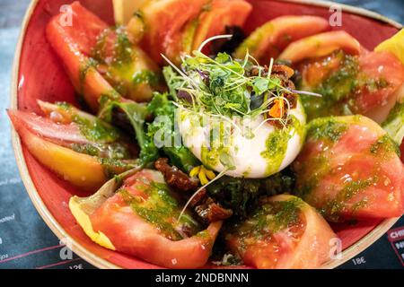 Ein Bild eines Burrata-Käsesalats gefüllt mit saftigen Tomaten, gekrönt mit Pesto-Dressing Stockfoto